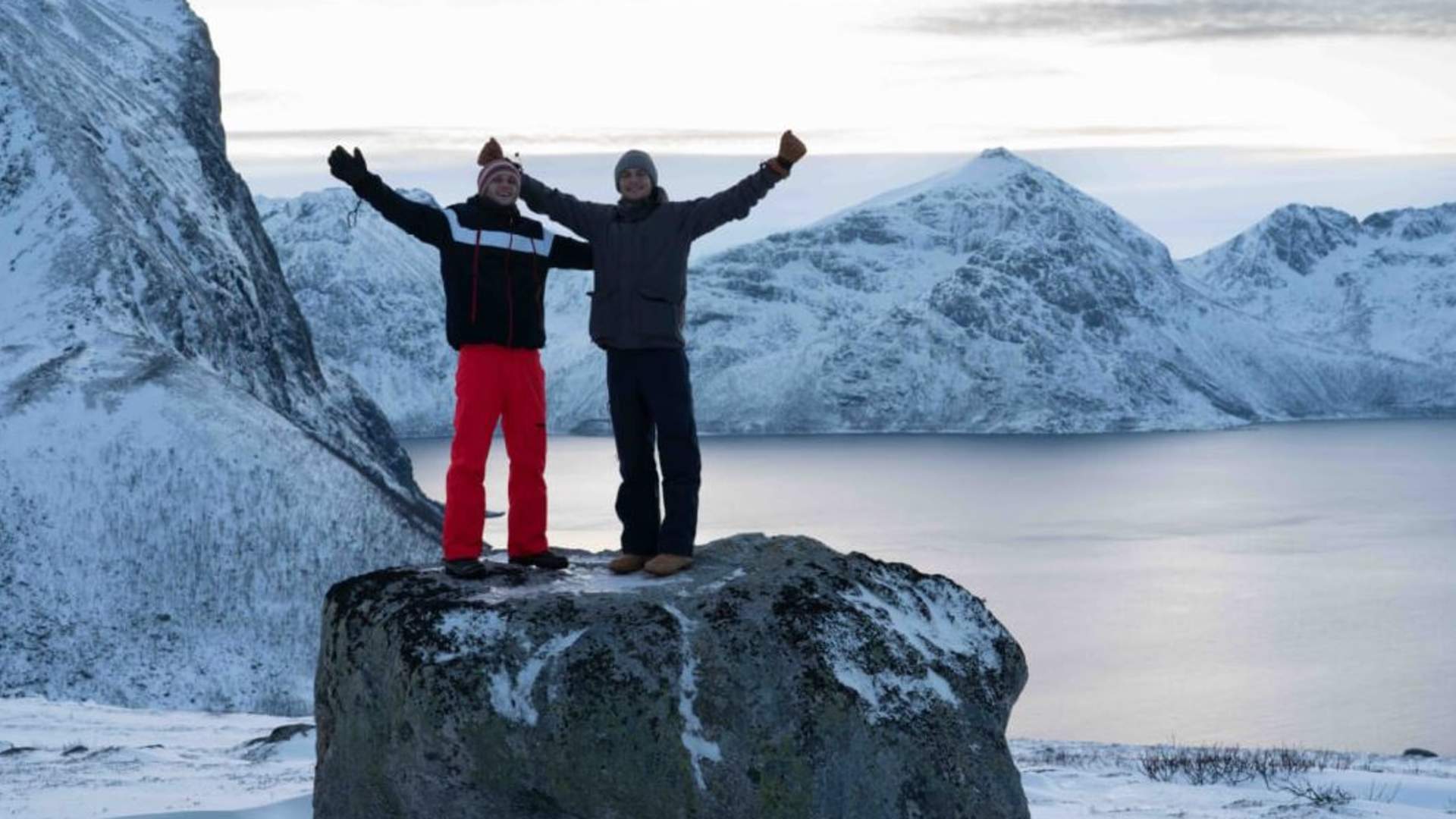 Two guests take a picture in front of the winter mountains and fjord
