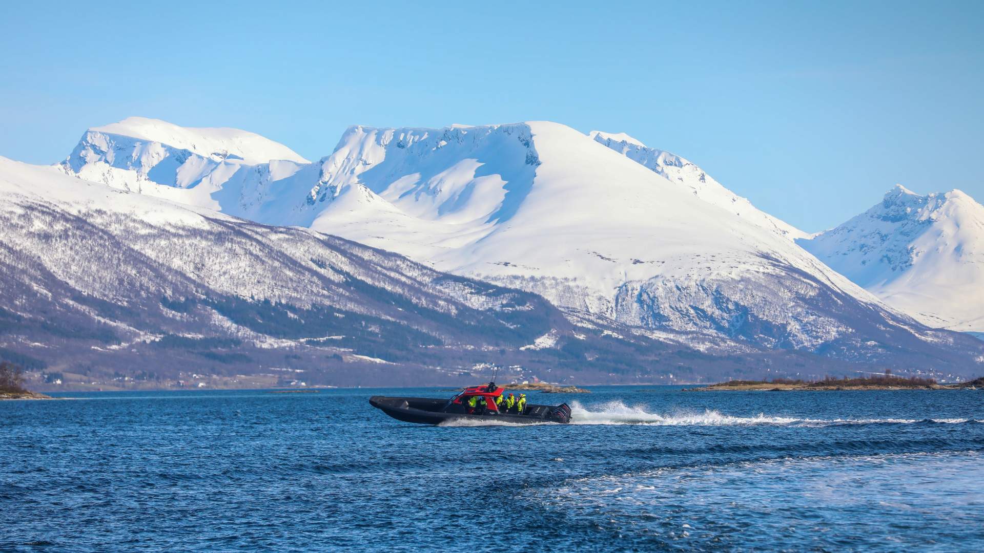 A RIB boat speeding on the water with snow covered mountains in the background