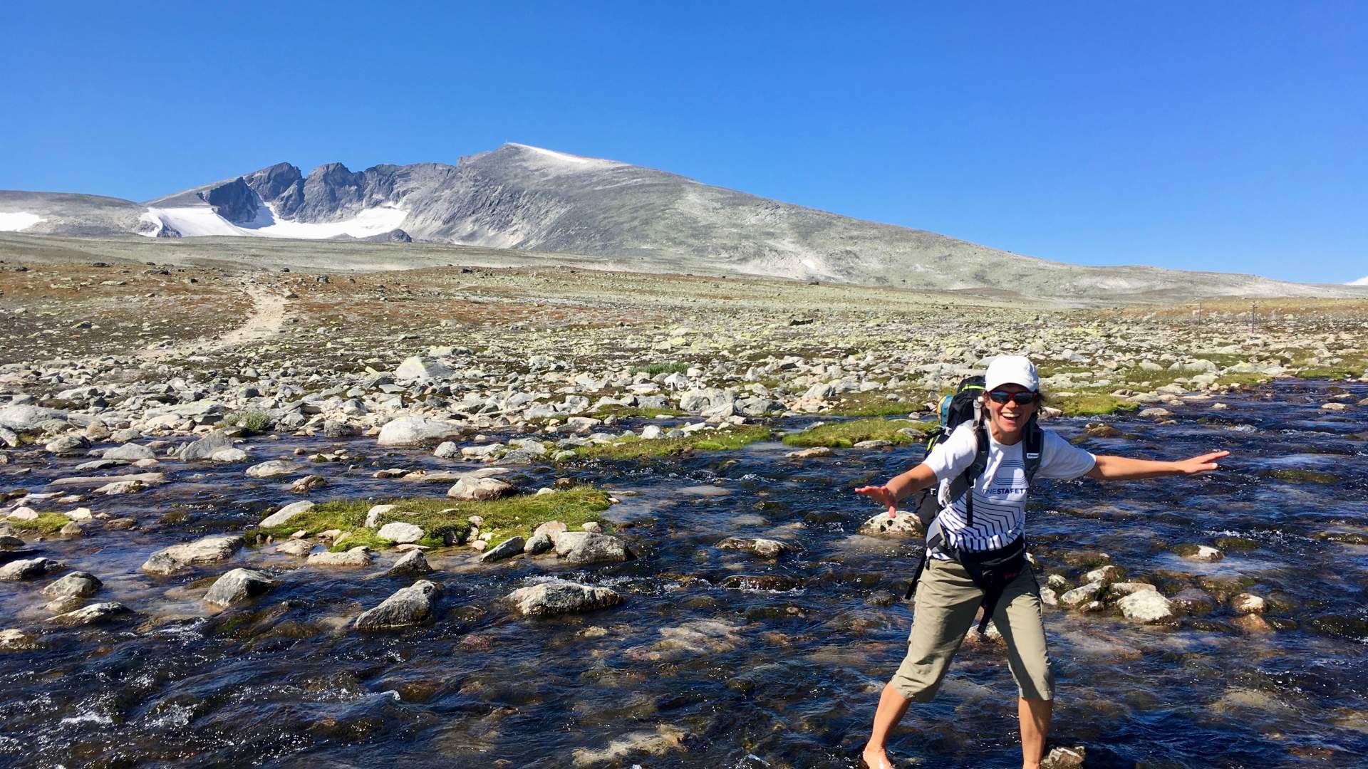 Turgåer krysser ei elv med Snøhetta i bakgrunn | Venabu Fjellhotell