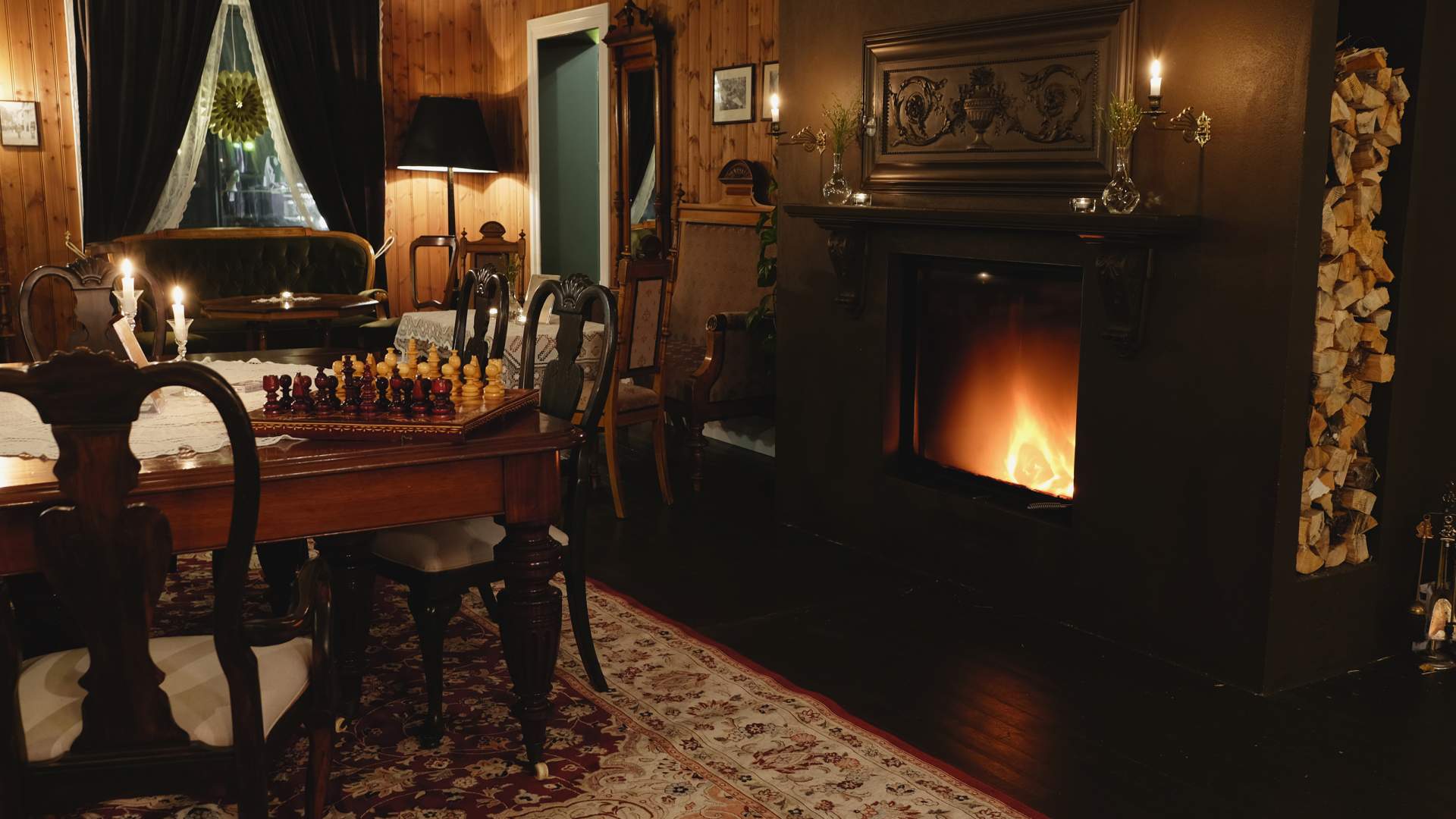 En mørk atmosfærisk bilde med fyr i peisen og et sjakkbrett på bordet bredvid.