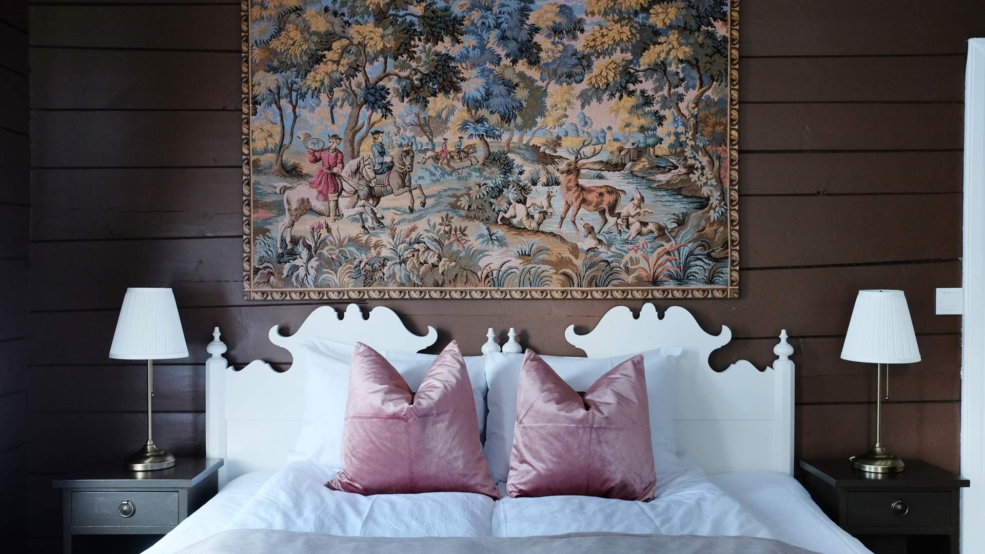 En seng i toner av rosa, med et stort broderi over sengen med historisk motiv.