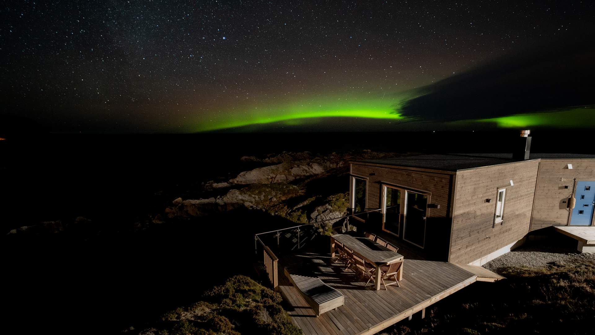 Nordlyset danser uti havet over hyttene på Runde Panorama.