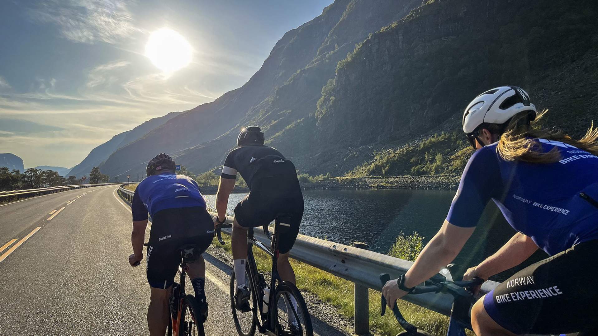 Tre syklister på tur med sol, fjell og vann