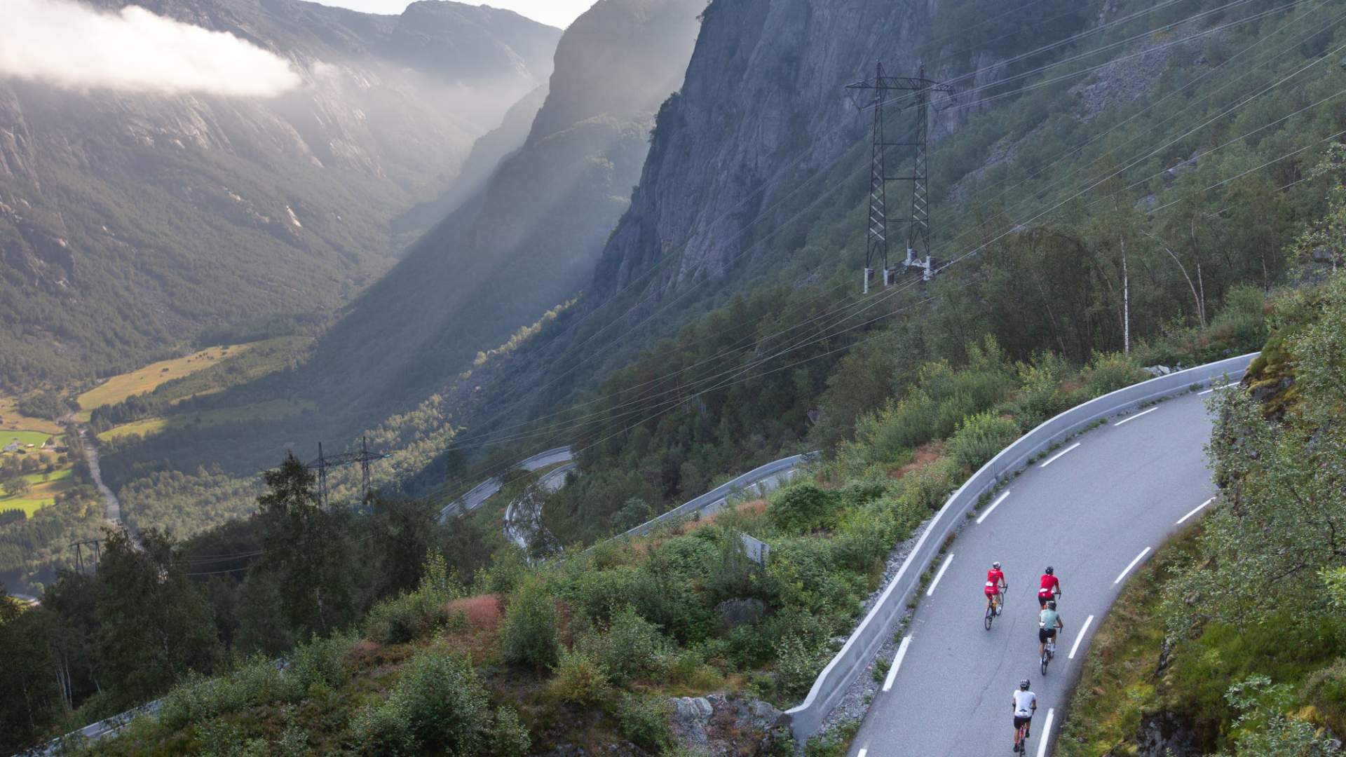 Norway Bike Experience. Tre syklister sykler opp en bakke med fjell og daler som utsikt