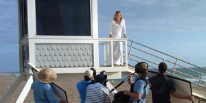 Woman standing on a structure on the beach with a filming crew in Fort Lauderdale