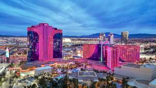 Exterior of Rio Las Vegas at night with pink lights on and the Las Vegas Strip in the background.