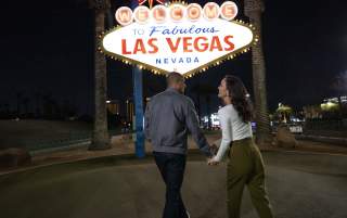 A couple holding hands at the famous "Welcome to Las Vegas" sign at night.