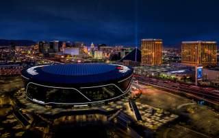 An aerial view of Allegiant Stadium at night with the Las Vegas Strip in the background.