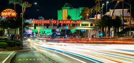 A front view of the illuminated Welcome to Laughlin sign at night with resorts in the background.