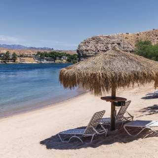 A serene beach at Harrah's Laughlin Beach with palapas and seats on the riverfront.
