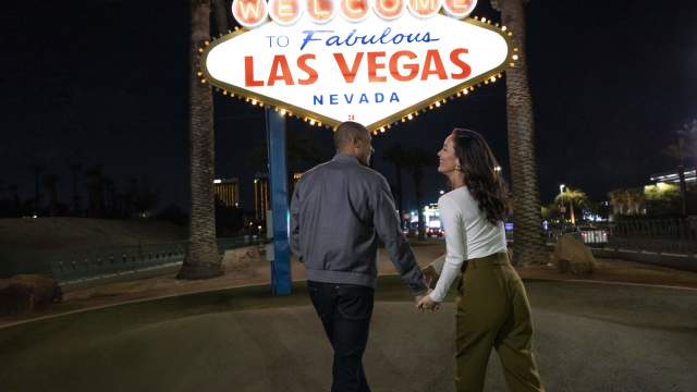 A couple holding hands at the famous "Welcome to Las Vegas" sign at night.