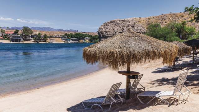 A serene beach at Harrah's Laughlin Beach with palapas and seats on the riverfront.