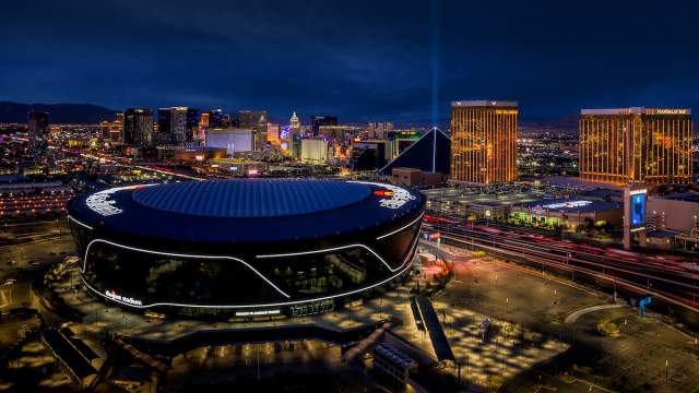 An aerial view of Allegiant Stadium at night with the Las Vegas Strip in the background.