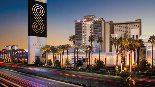 A view of the SAHARA Las Vegas resort at night with palm trees in front.