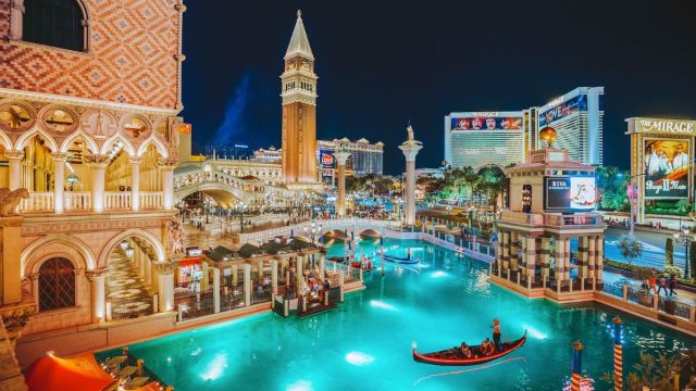 A couple in a gondola floating in the lit up canal at night in front of the Venetian hotel
