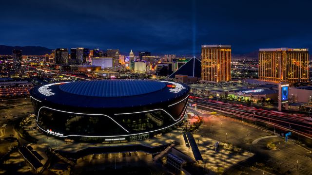 An aerial view of Allegiant Stadium at night with the Las Vegas Strip in the background.