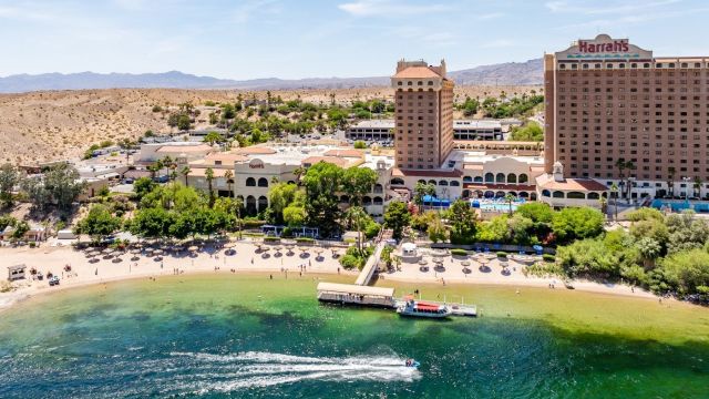 Aerial view of Harrah's Laughlin resort on the Colorado River with a sandy beach, pool area, and jet skier in turquoise water.