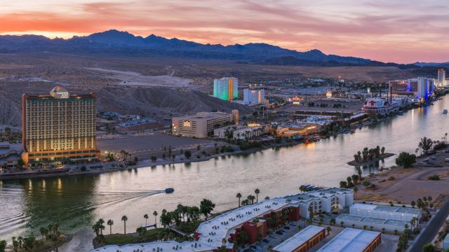 Aerial sunset view of the Colorado River lined with Laughlin casino resorts, mountains, and desert terrain.