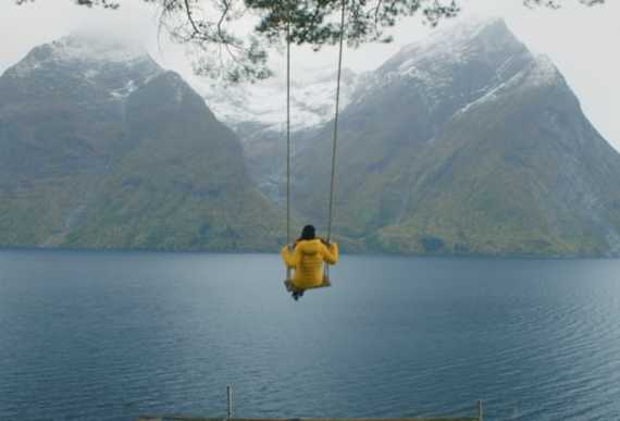 A person on a swing with views of snow-clad mountains and the Hjørundfjord in Fjord Norway