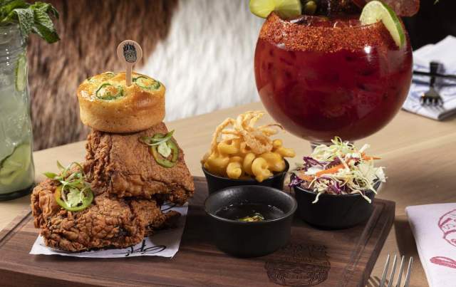 Two pieces of fried chicken stacked on top of each other, a small bowl of french fries, a small bowl of coleslaw and a large cocktail.
