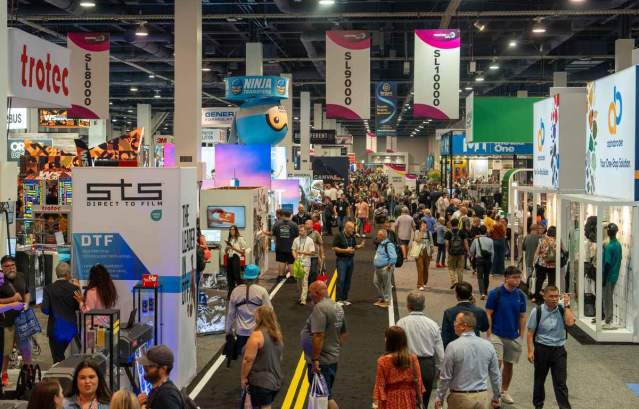 A group of people walking through a printing expo with booths in Las Vegas.