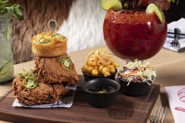 Two pieces of fried chicken stacked on top of each other, a small bowl of french fries, a small bowl of coleslaw and a large cocktail.