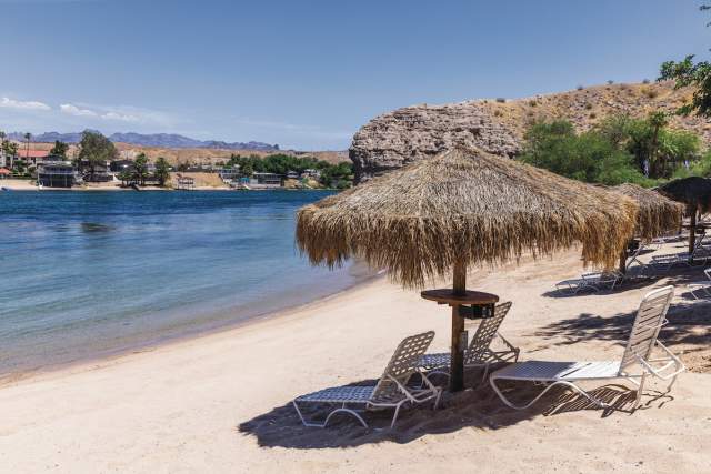 A serene beach at Harrah's Laughlin Beach with palapas and seats on the riverfront.