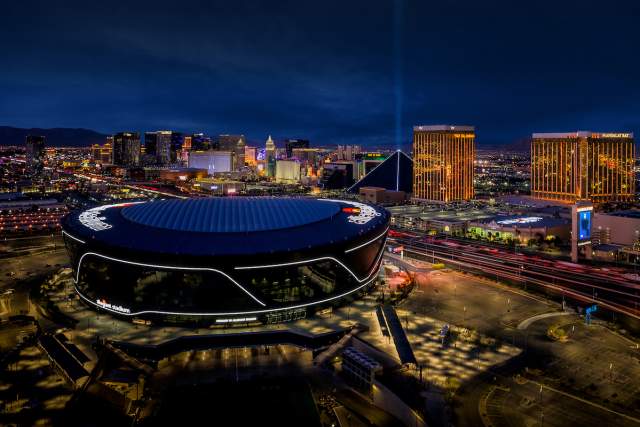 An aerial view of Allegiant Stadium at night with the Las Vegas Strip in the background.