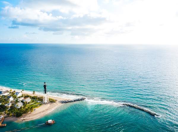 The Hillsboro Lighthouse stands at the edge of the Hillsboro Inlet, surrounded by the crystal blue Florida coastline