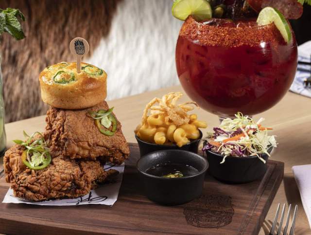 Two pieces of fried chicken stacked on top of each other, a small bowl of french fries, a small bowl of coleslaw and a large cocktail.