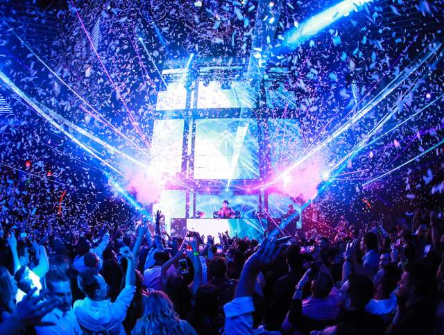 People dancing in a nightclub with laser lights and confetti falling from the ceiling