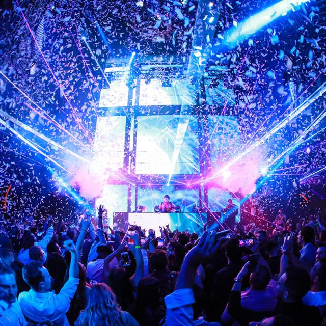 People dancing in a nightclub with laser lights and confetti falling from the ceiling