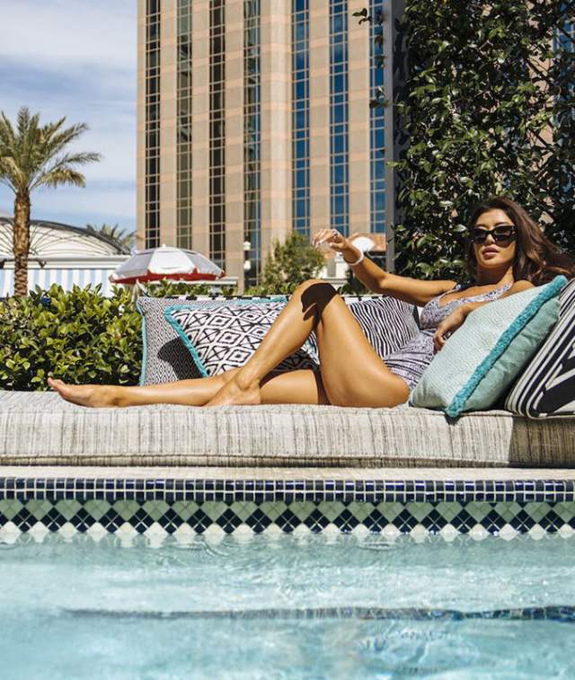A woman laying down on an outdoor couch poolside.