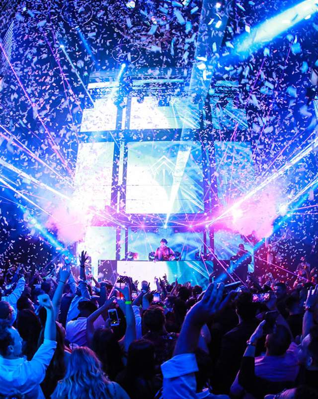 People dancing in a nightclub with laser lights and confetti falling from the ceiling