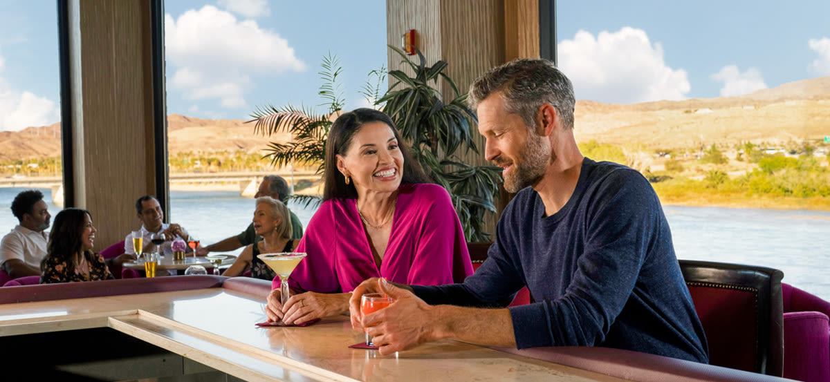 A couple enjoying some delicious cocktails in Laughlin with the beautiful Colorado river behind them.