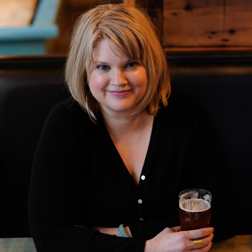 Heather Van Dyke of Harmony Brewing sitting at a table holding a beer.