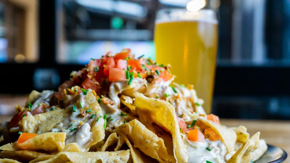 A plate piled with duck nachos with a beer in the background at Brewery Vivant.