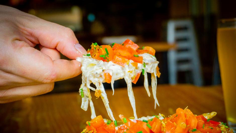 A hand pulling a chip away from a plate of Brewery Vivant's duck nachos.