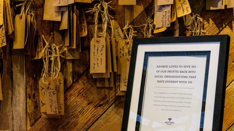 Framed sign at Adored Boutique highlighting its commitment to donate 15% of profits to local causes.