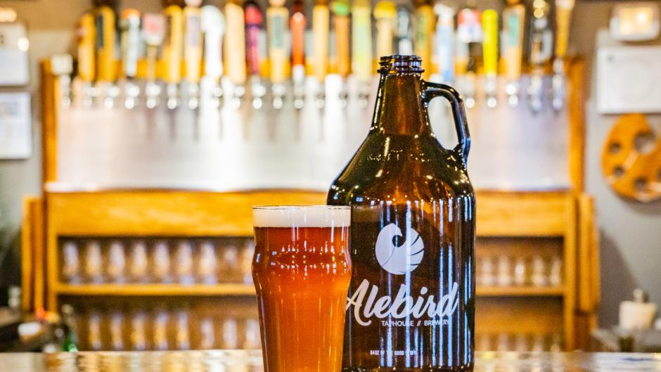 A glass of beer next to a growler container with the Alebird logo on it.