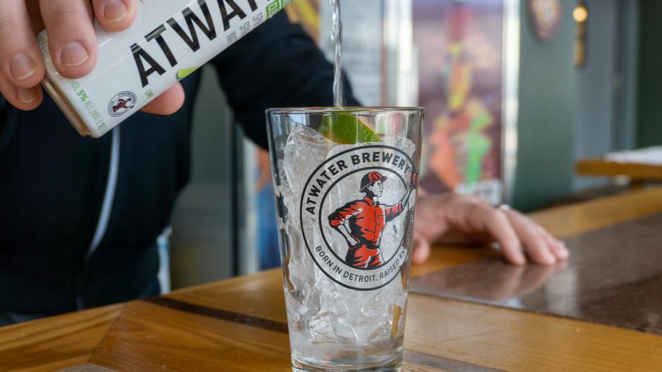 Pouring hard seltzer from a can into an Atwater Brewery branded pint glass.