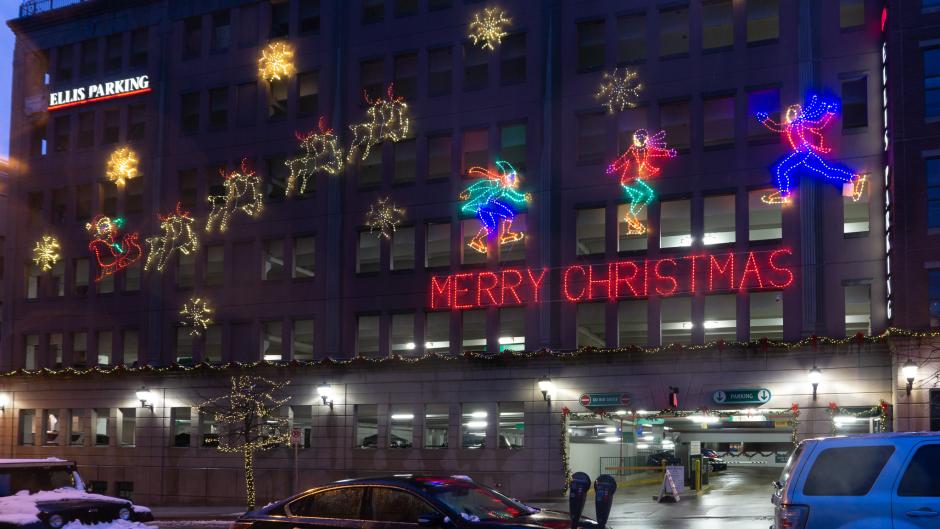 Holiday lights on an Ellis Parking ramp that read "Merry Christmas" and show ice skaters and Santa's sleigh.