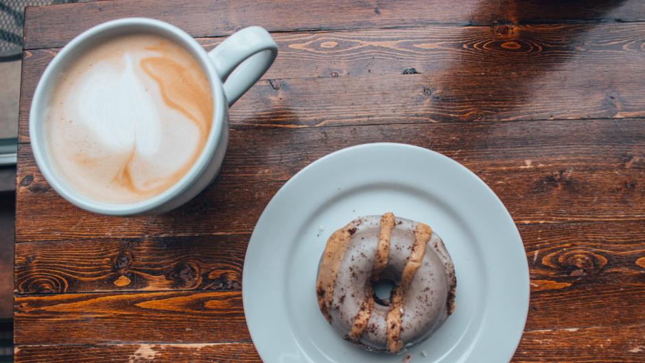 A donut on a plate next to a hot latte at the Lantern.
