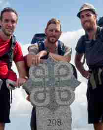 Three men standing around a milestone on the pilgrimage path to Trondheim, Norway
