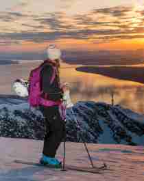 Two women with skis enjoying the view of mountains and fjord from the top of a mountain in Narvik, Northern Norway