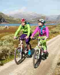 Dos personas pedalean en bicicleta por Rallarvegen (o la ruta de los peones camineros), en la Noruega de los fiordos, durante un día soleado.