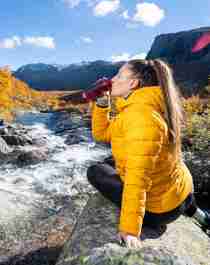 Woman drinking water from a river, Hemsedal, Norway.