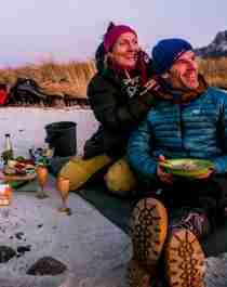 Two campers having a cosy campfire dinner on a beach in the evening light