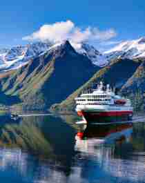 Et Hurtigruten-skib på Hjørundfjorden i Fjord Norge, omgivet af sneklædte fjelde