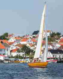 A wooden sailboat sailing in front of white-painted wooden houses in Risør, Southern Norway